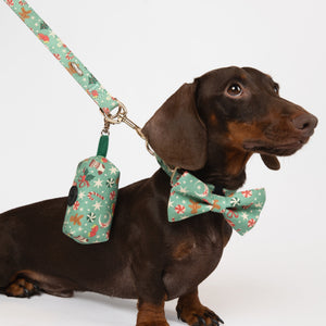 Dog wearing a floral bow tie and holding a floral-patterned leash and toy on a white background
