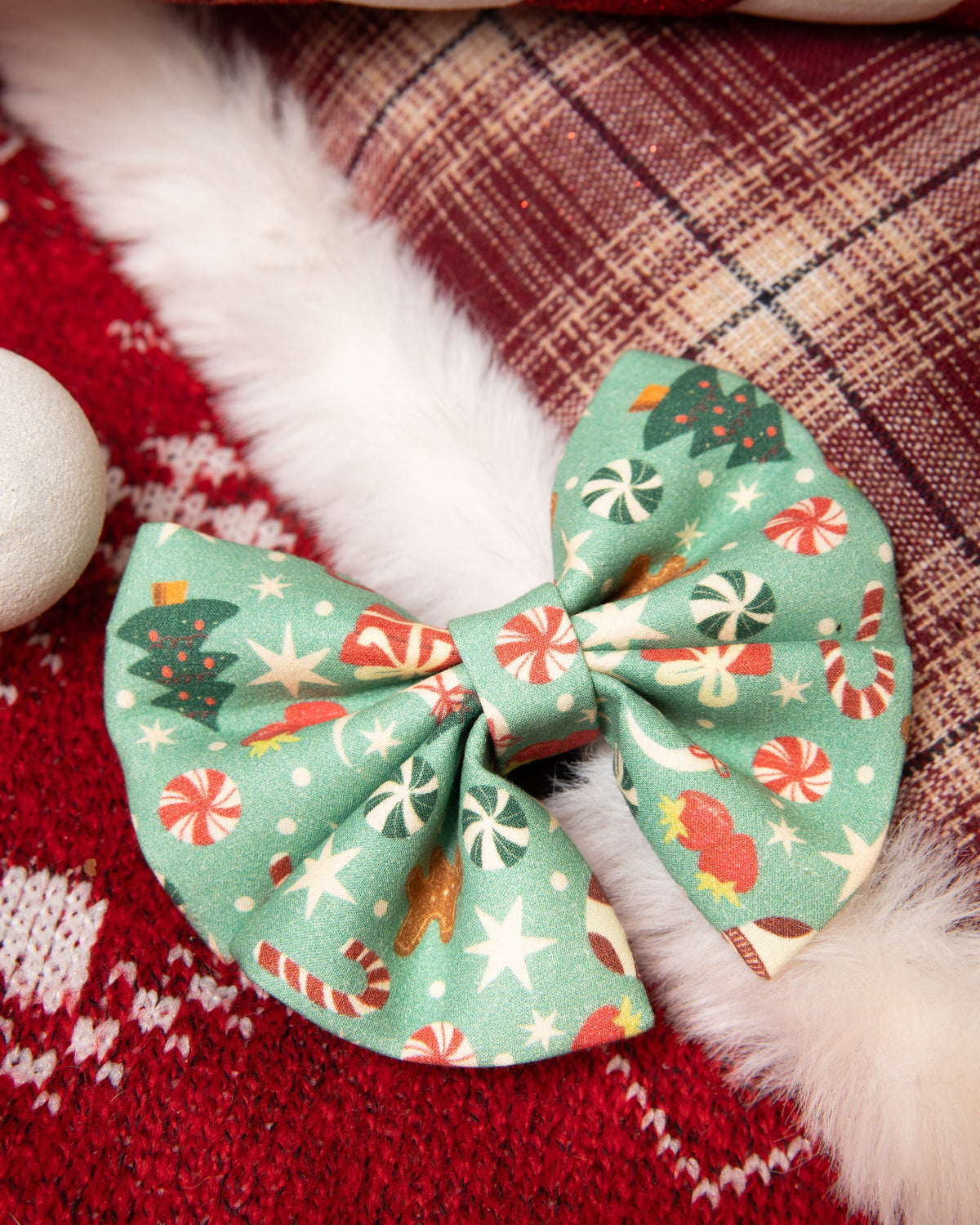 Christmas-themed bow on a red fabric background with candy cane and plaid patterns.